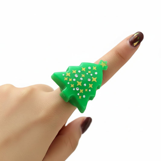 Hand wearing a green Christmas tree-shaped ring with gold stars against a blurred light background