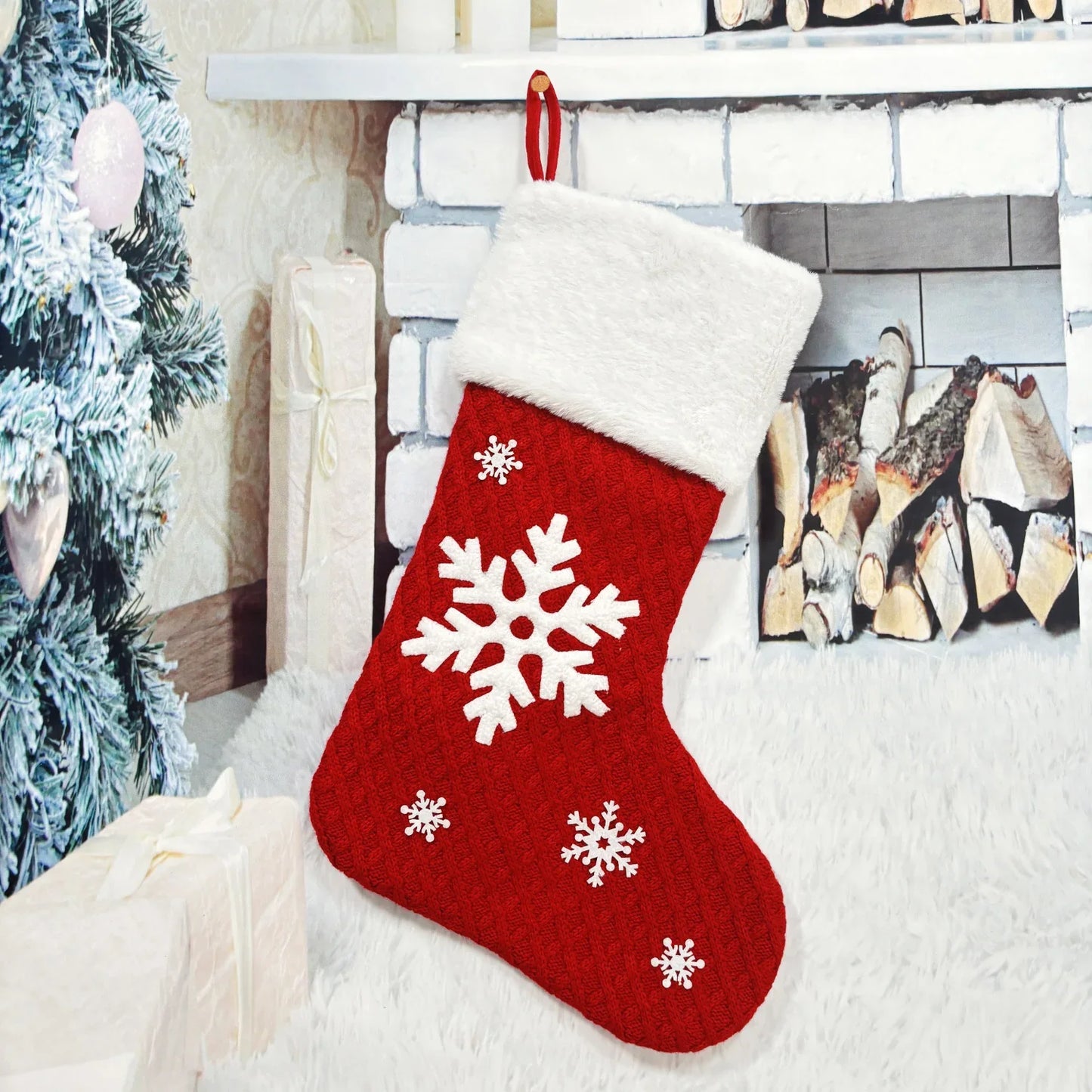 Red Christmas stocking with white snowflakes hanging by a fireplace.
