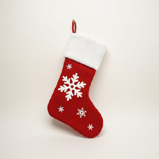 Red Christmas stocking with white snowflakes hanging by a fireplace.