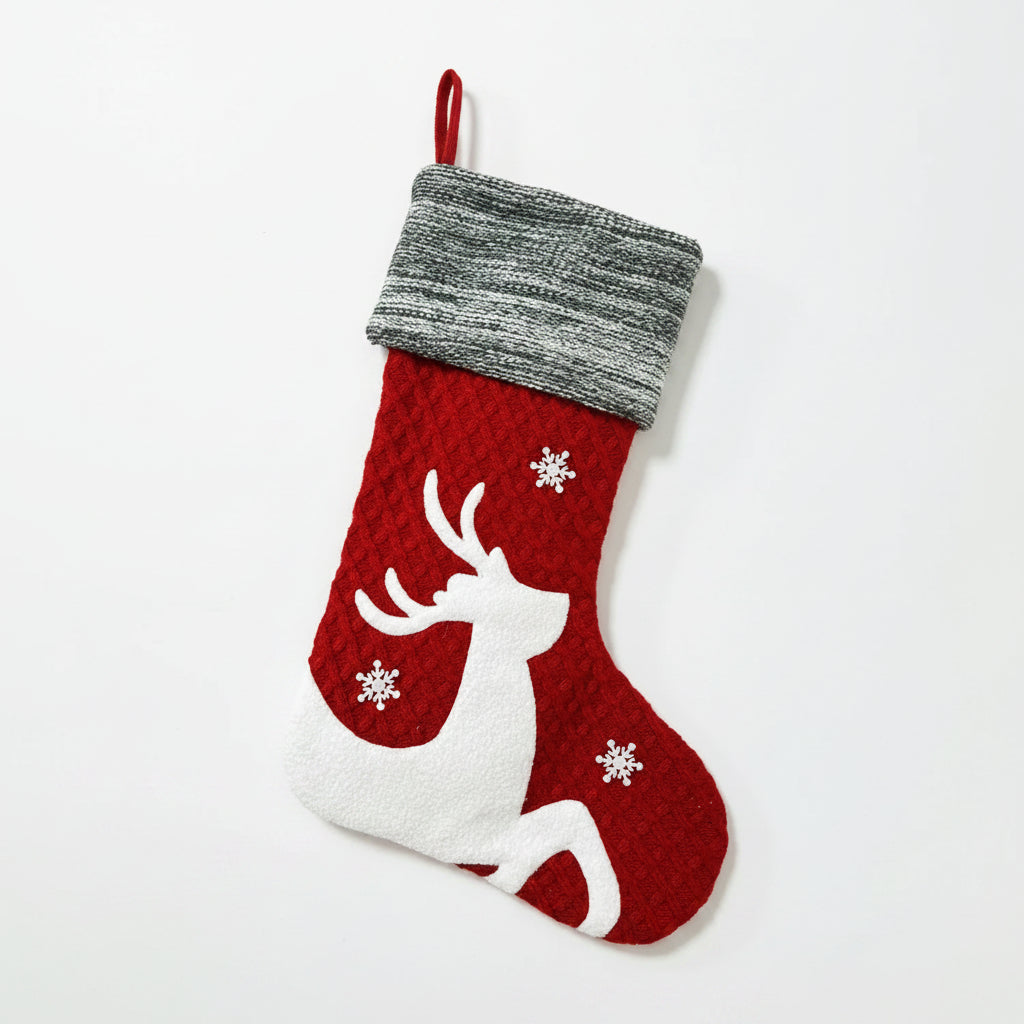 Red Christmas stocking with reindeer design hanging by a fireplace with festive decorations.