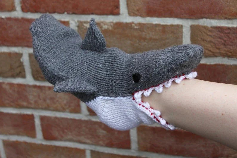 Knitted shark slipper on a person's foot against a brick wall background