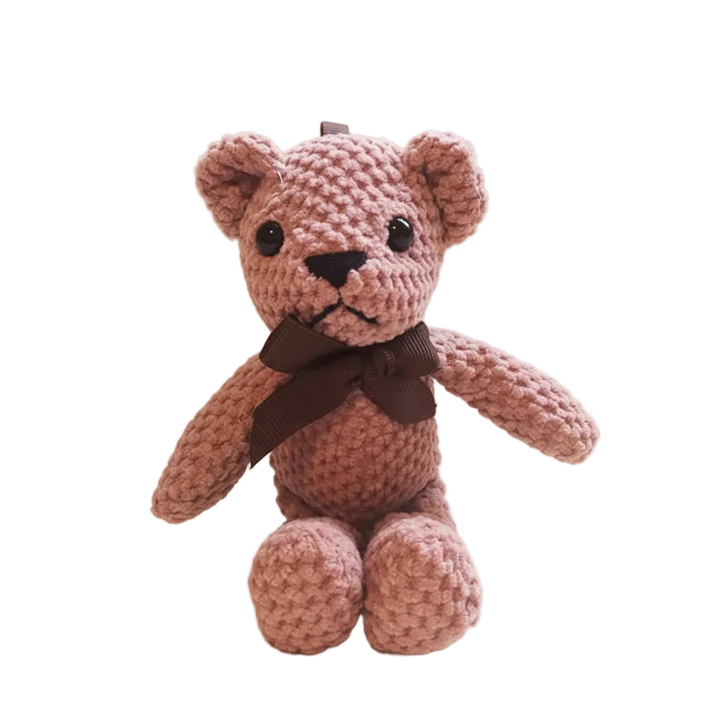 Pink knitted teddy bear with a brown bow tie on a wooden surface.