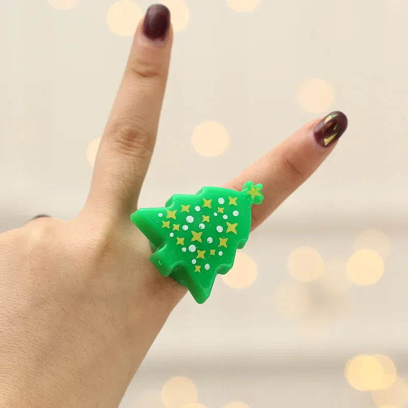 Hand wearing a green Christmas tree-shaped ring with gold stars against a blurred light background